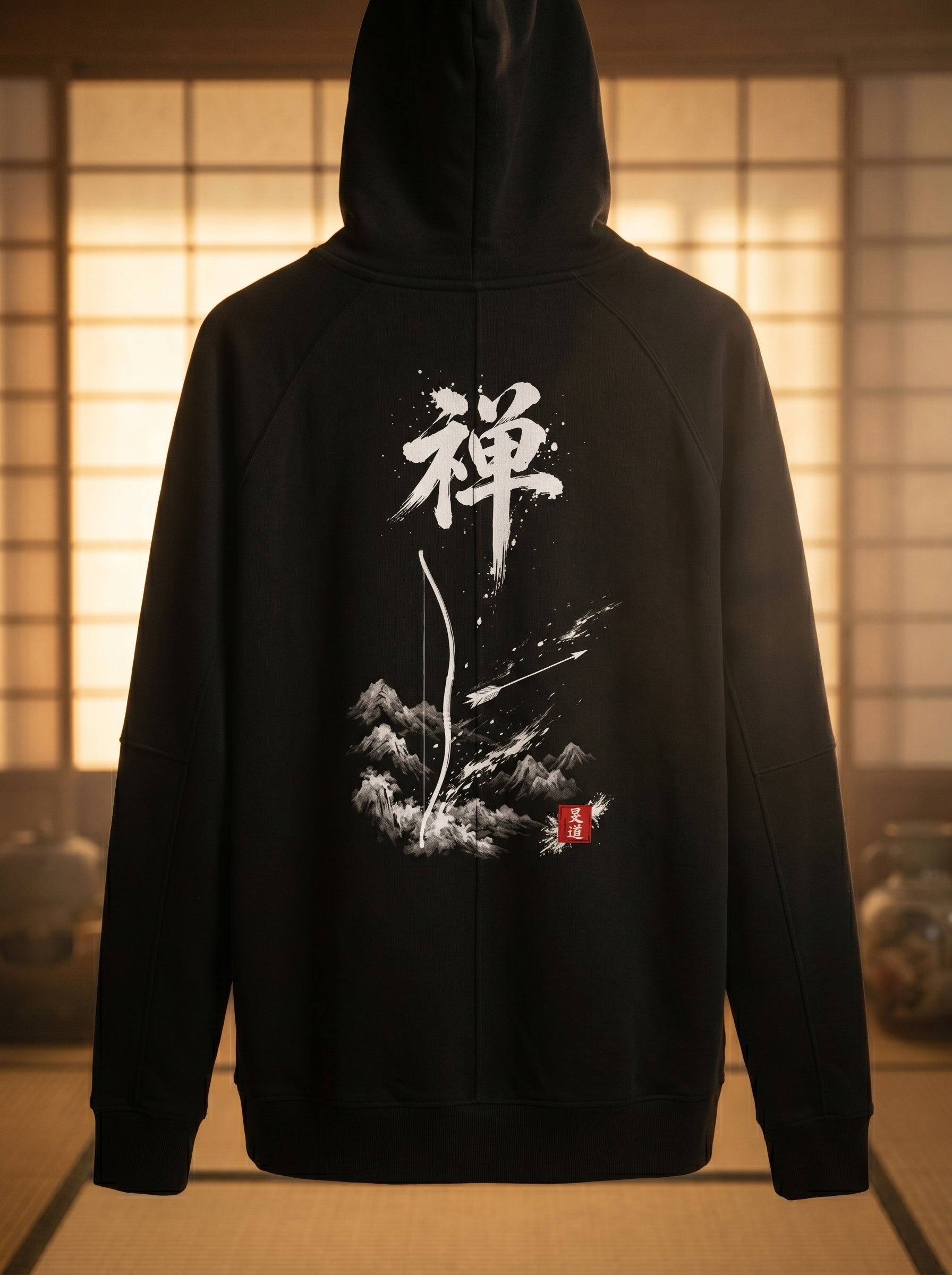 Overhead flat lay of black hoodie back with Zen 禅 Sumi-e calligraphy and Kyūdō bow-and-arrow graphic, surrounded by ink stone, calligraphy brush, arrows and red hanko seal on dark wood, MINDŌ Studio
