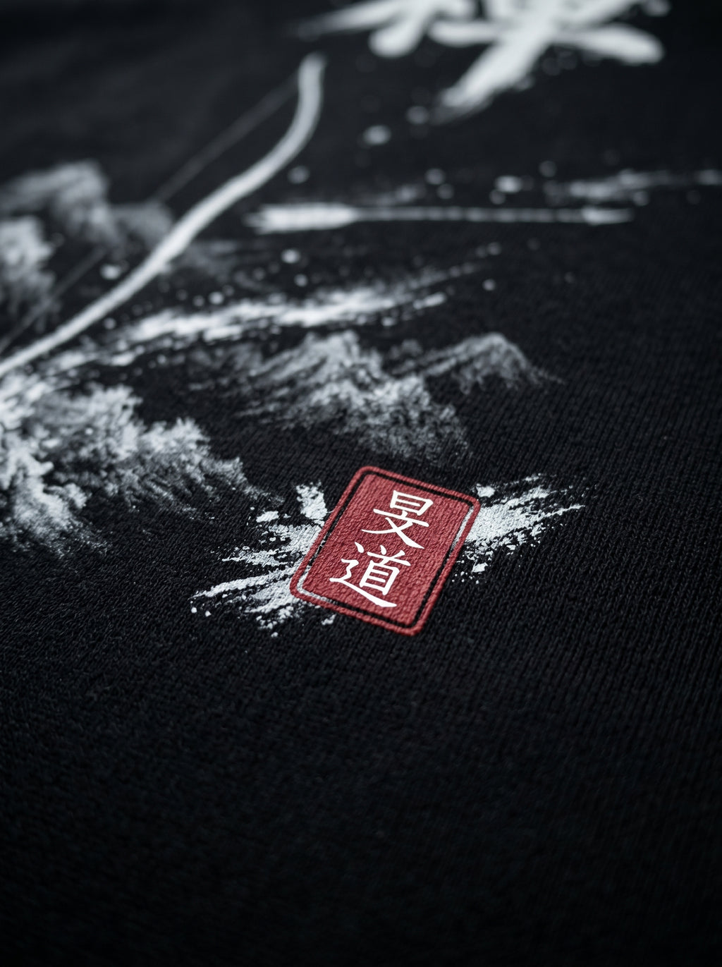 Extreme close-up macro of red Hanko seal with Japanese kanji on black hoodie fabric, Sumi-e ink brushwork mountain landscape visible in background, MINDŌ Studio craftsmanship detail
